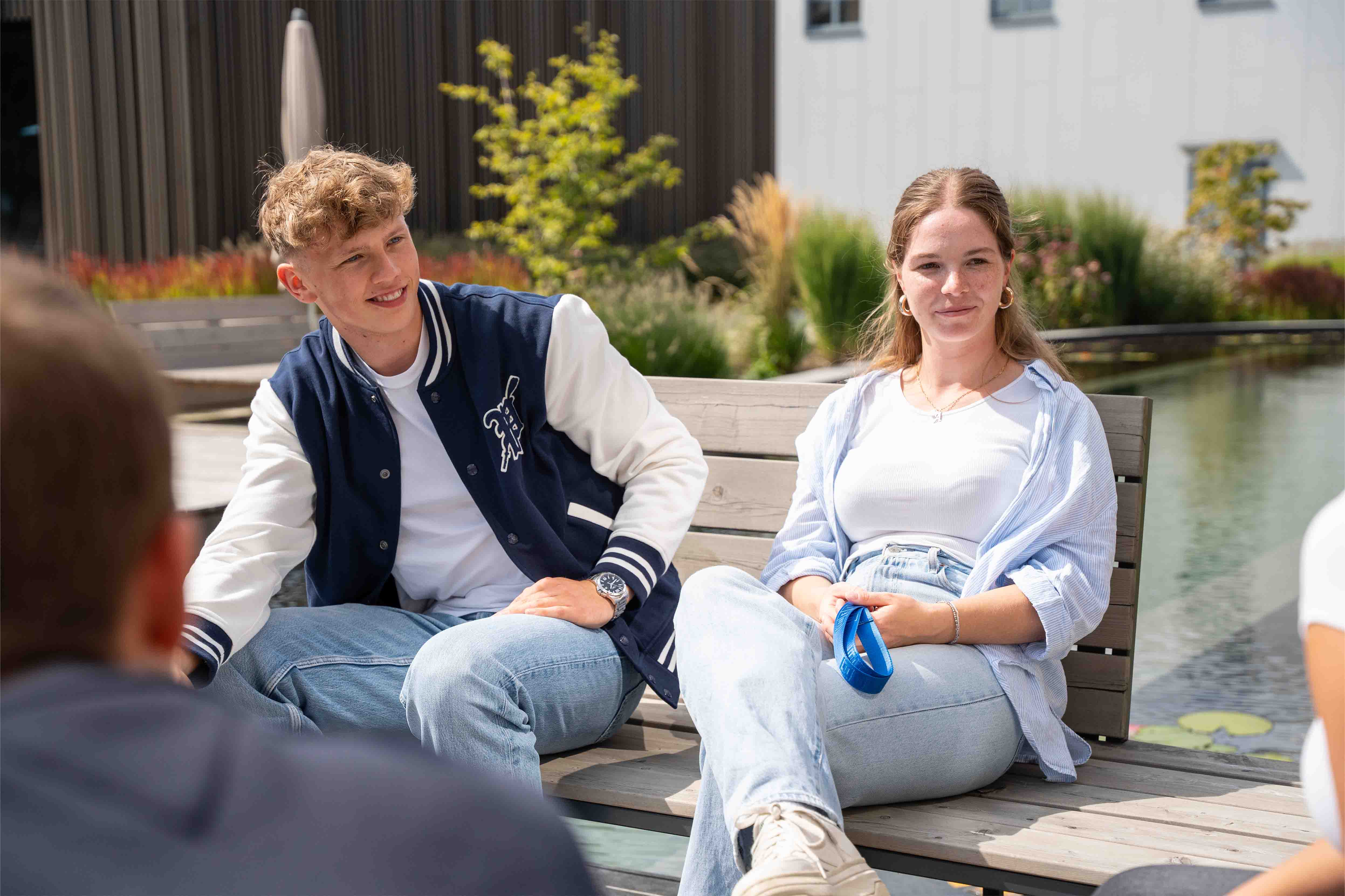 A young man and a young woman sit relaxed and smiling by the pool.
