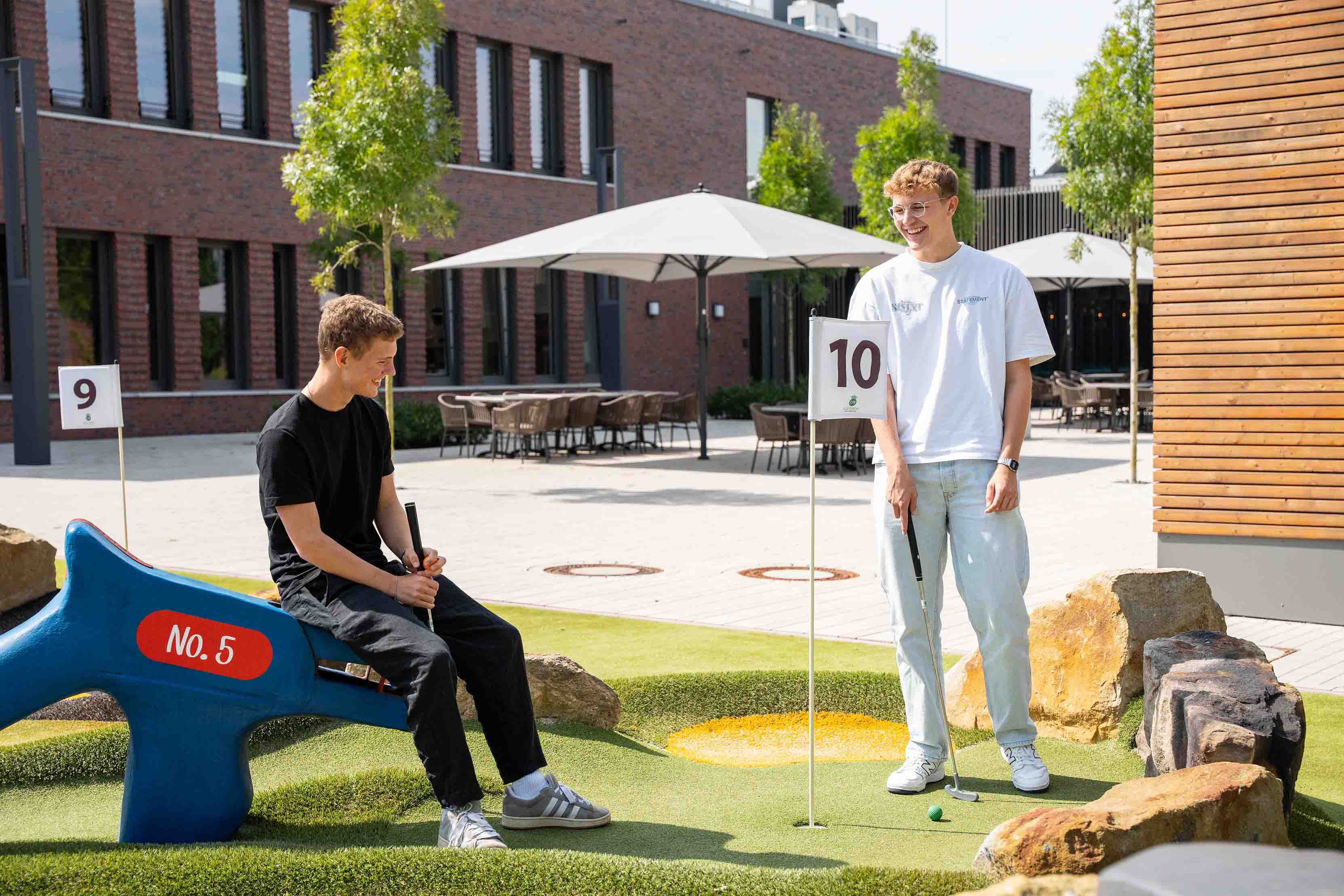 Two young men are playing mini golf together and laughing.